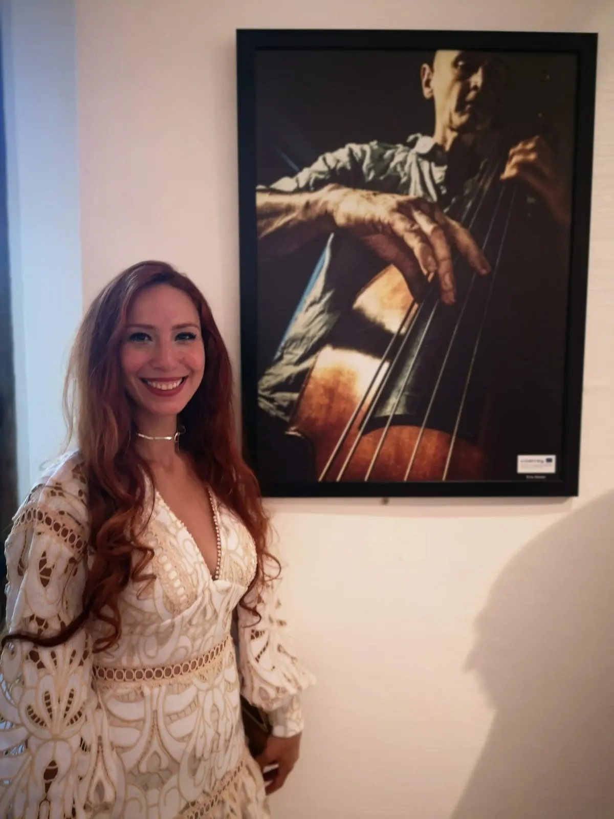 Frau steht neben gerahmtem Foto eines Kontrabassspielers an einer weißen Galeriewand