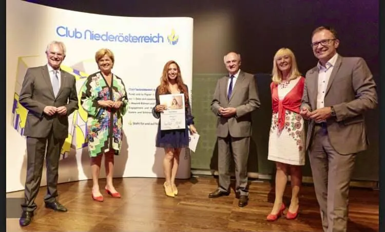 Gruppenfoto mit sechs Personen vor Club-Niederösterreich-Wand, Frau in der Mitte hält Urkunde