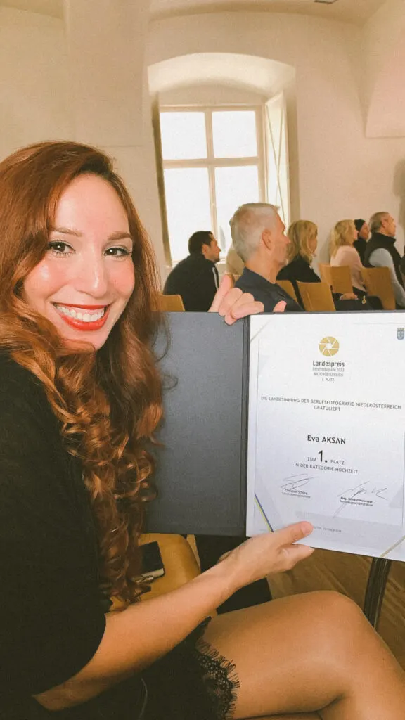 Lächelnde Frau zeigt aufgeschlagene Urkundenmappe des Landespreises Berufsfotografie 2023 im Veranstaltungssaal