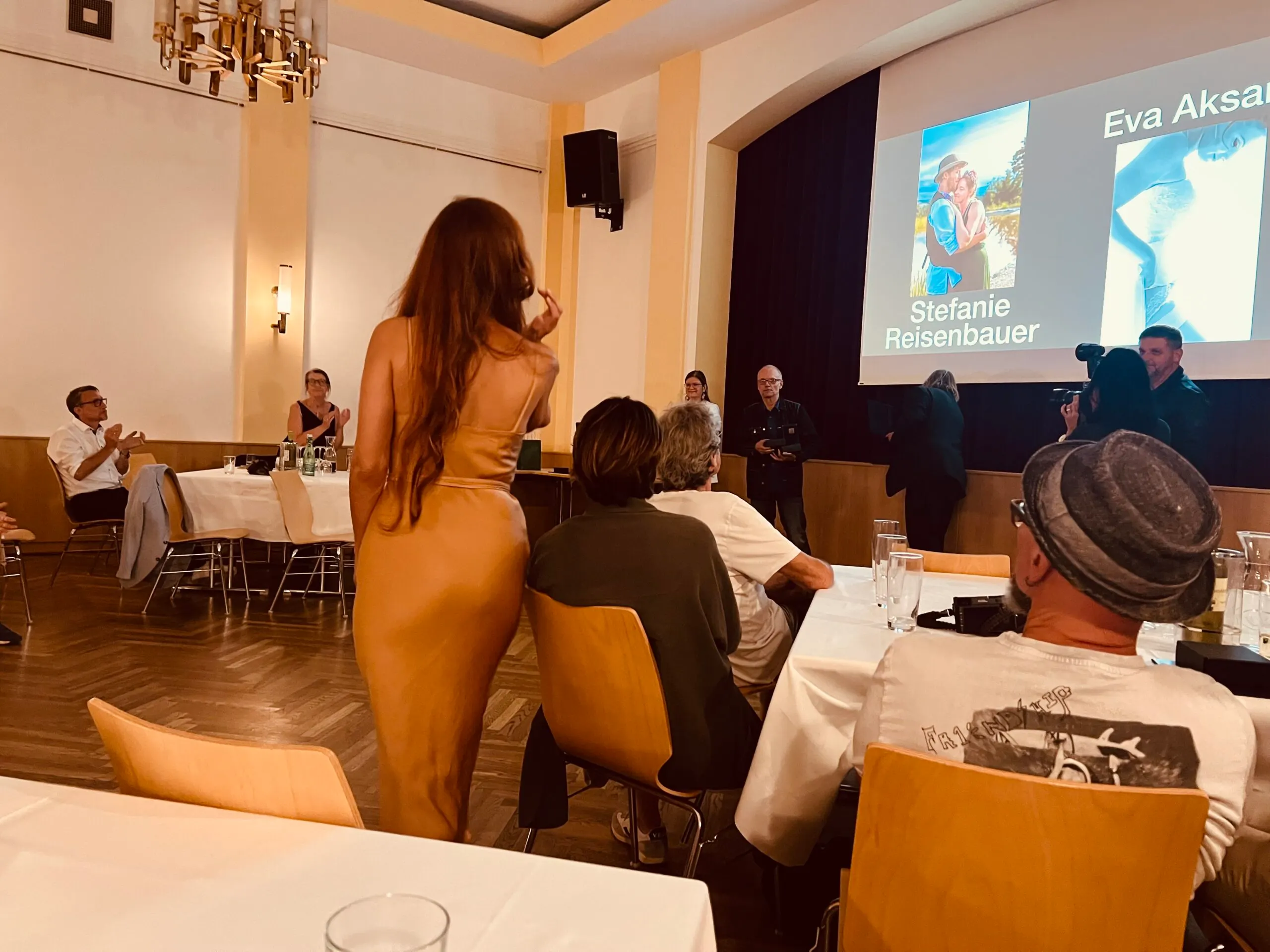 Saal während der Preisverleihung, Leinwand zeigt Fotos mit Namen Stefanie Reisenbauer und Eva Aksan