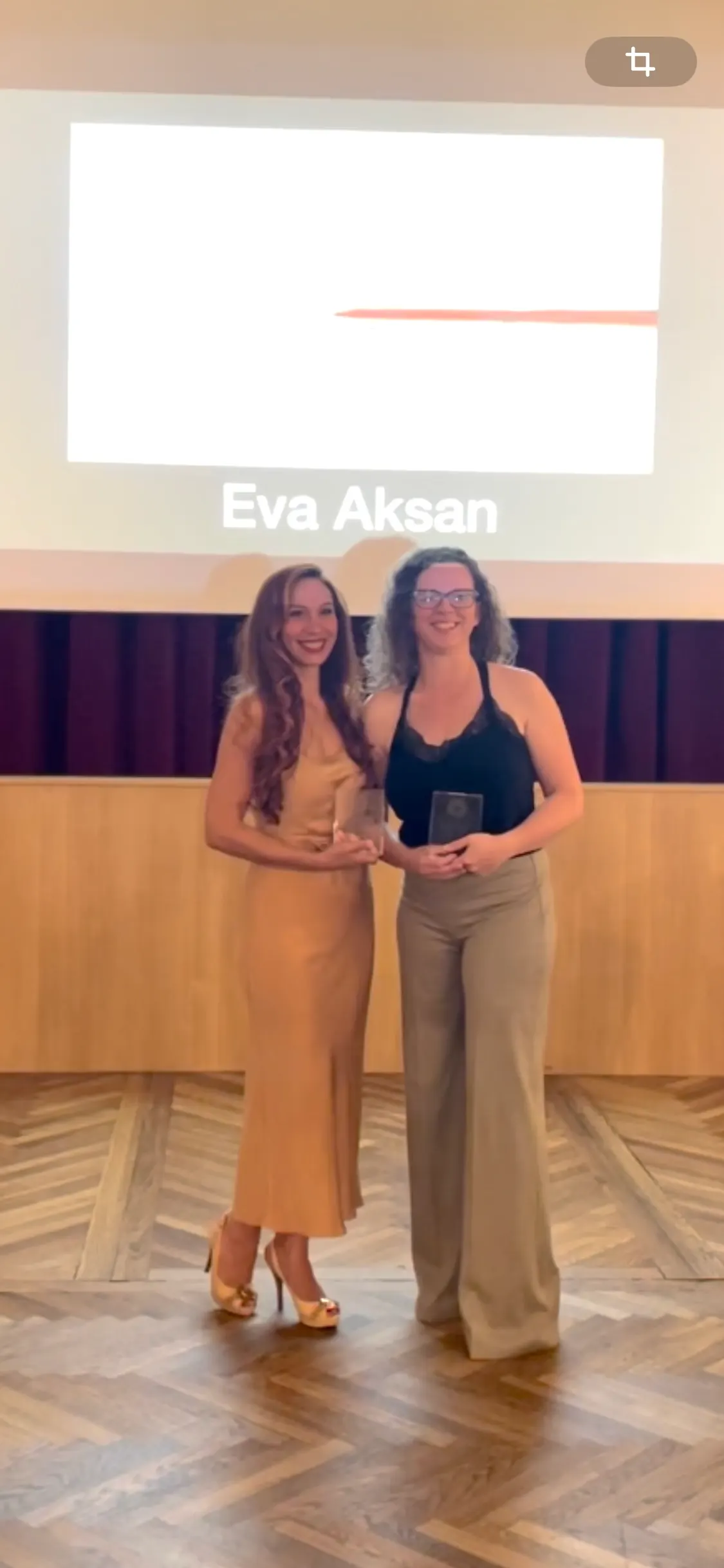 Zwei Frauen mit Glastrophäen, auf der Leinwand darüber steht der Name Eva Aksan