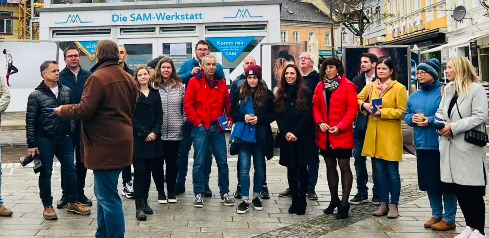 Besuchergruppe bei einer Vernissage vor der SAM-Werkstatt, links Ausstellungstafeln mit Fotografien