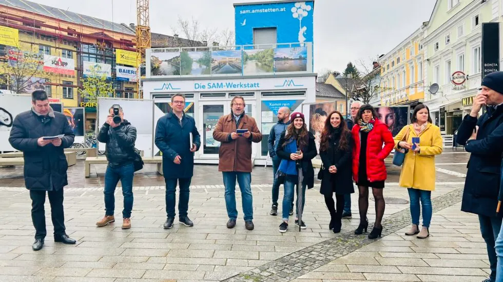 Gäste einer Freiluftausstellung vor der SAM-Werkstatt mit Fotopaneelen, ein Mann spricht zur Gruppe