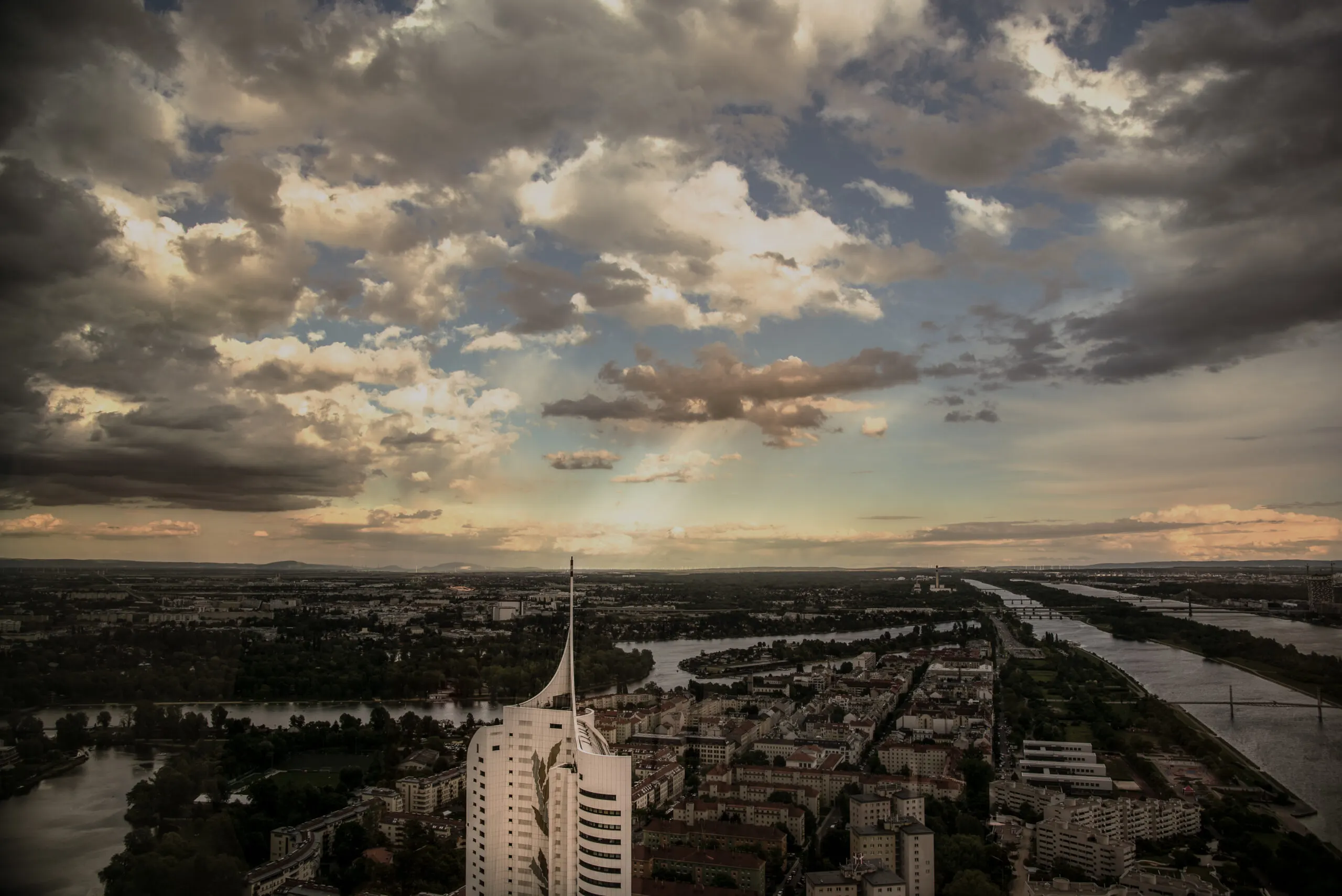 Blick von oben über Wien und die Donau mit markantem Hochhaus unter dramatischem Wolkenhimmel