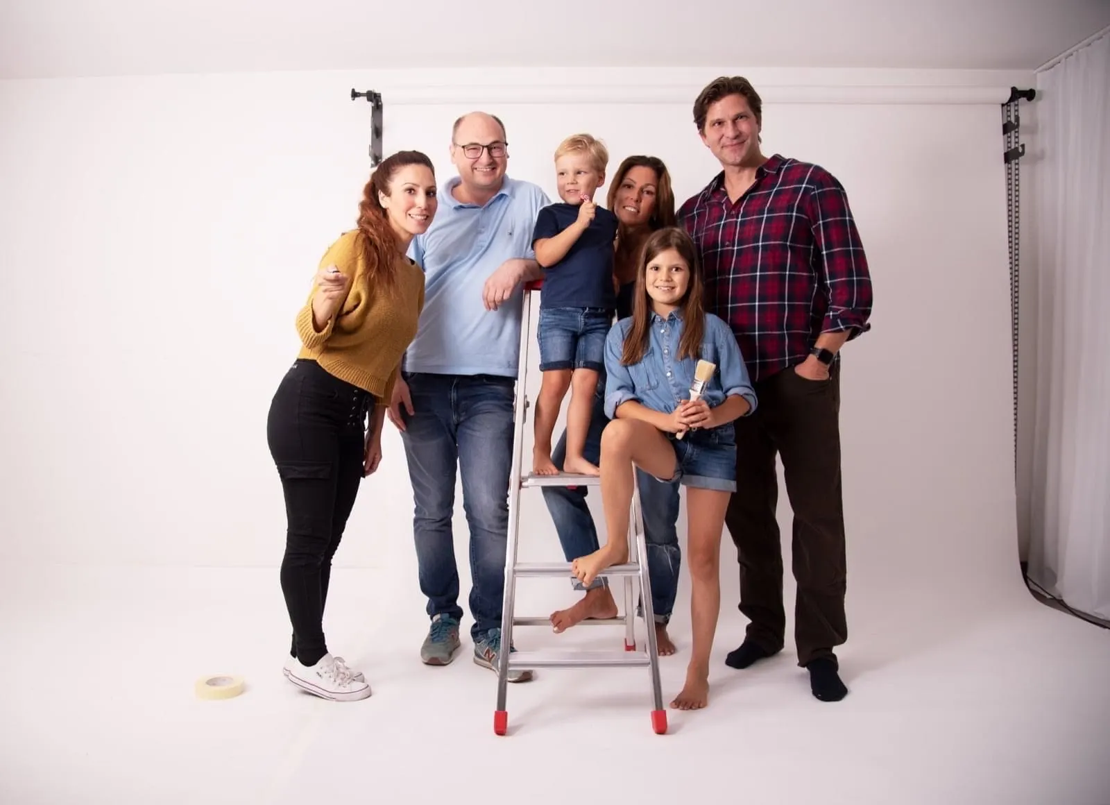 Familiengruppe mit Kindern und Malerpinsel auf Leiter im Fotostudio vor weißem Hintergrund
