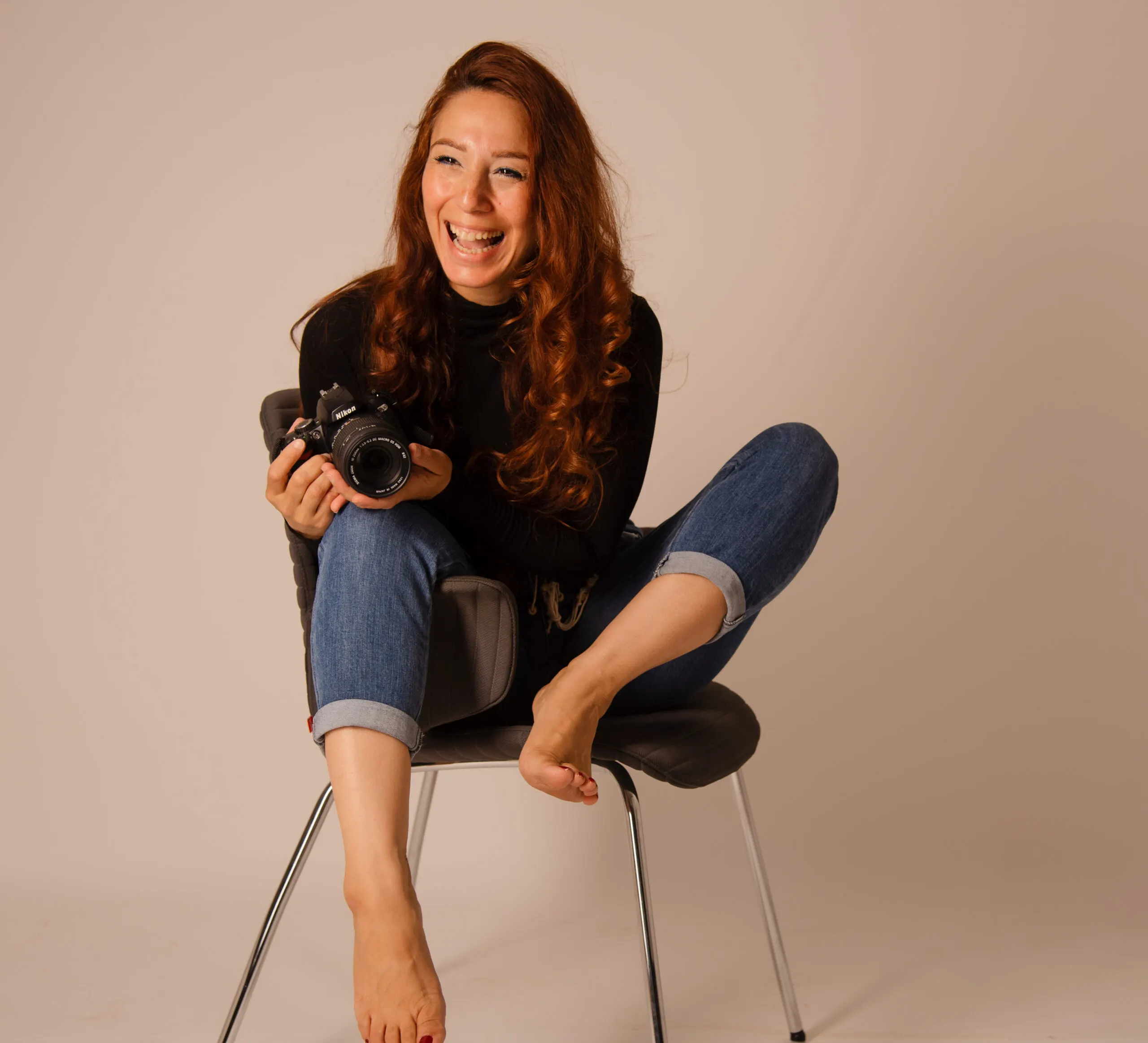 Eva Aksan lacht mit ihrer Nikon-Kamera in der Hand im Studio