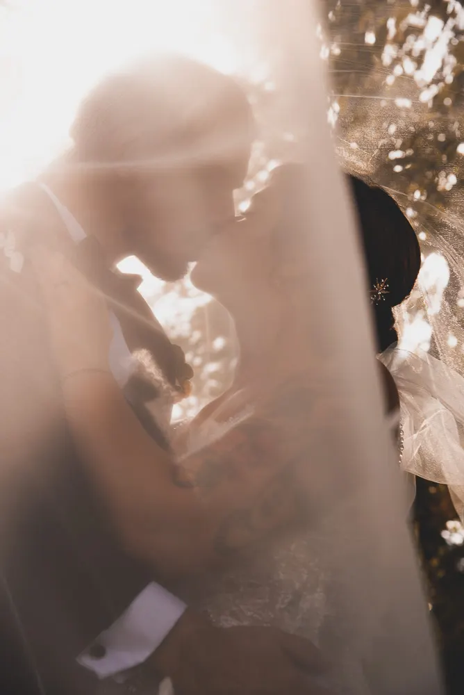 Kuss unter dem Schleier im goldenen Gegenlicht, Angis Arm mit Tattoo um ihren Mann gelegt.