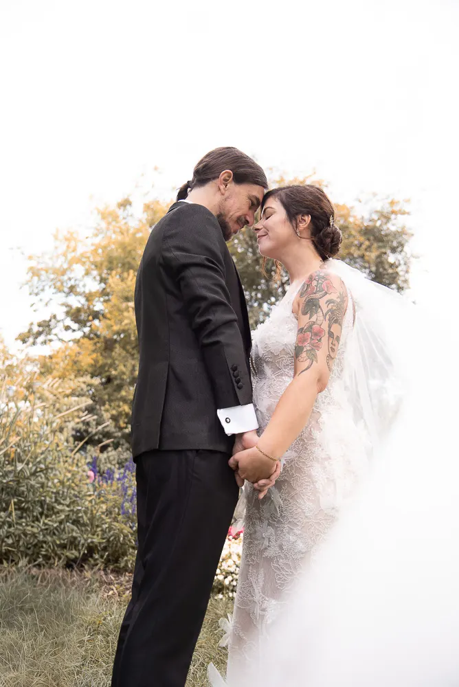 Stirn an Stirn stehen die beiden Hand in Hand im herbstlichen Garten, Angis Armtattoo im Blick.