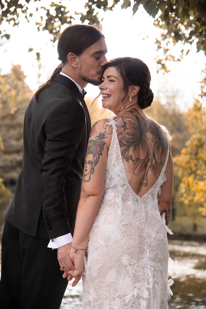 Er küsst Angis Schläfe, der tiefe Rückenausschnitt des Kleides zeigt ihr großes Rückentattoo.