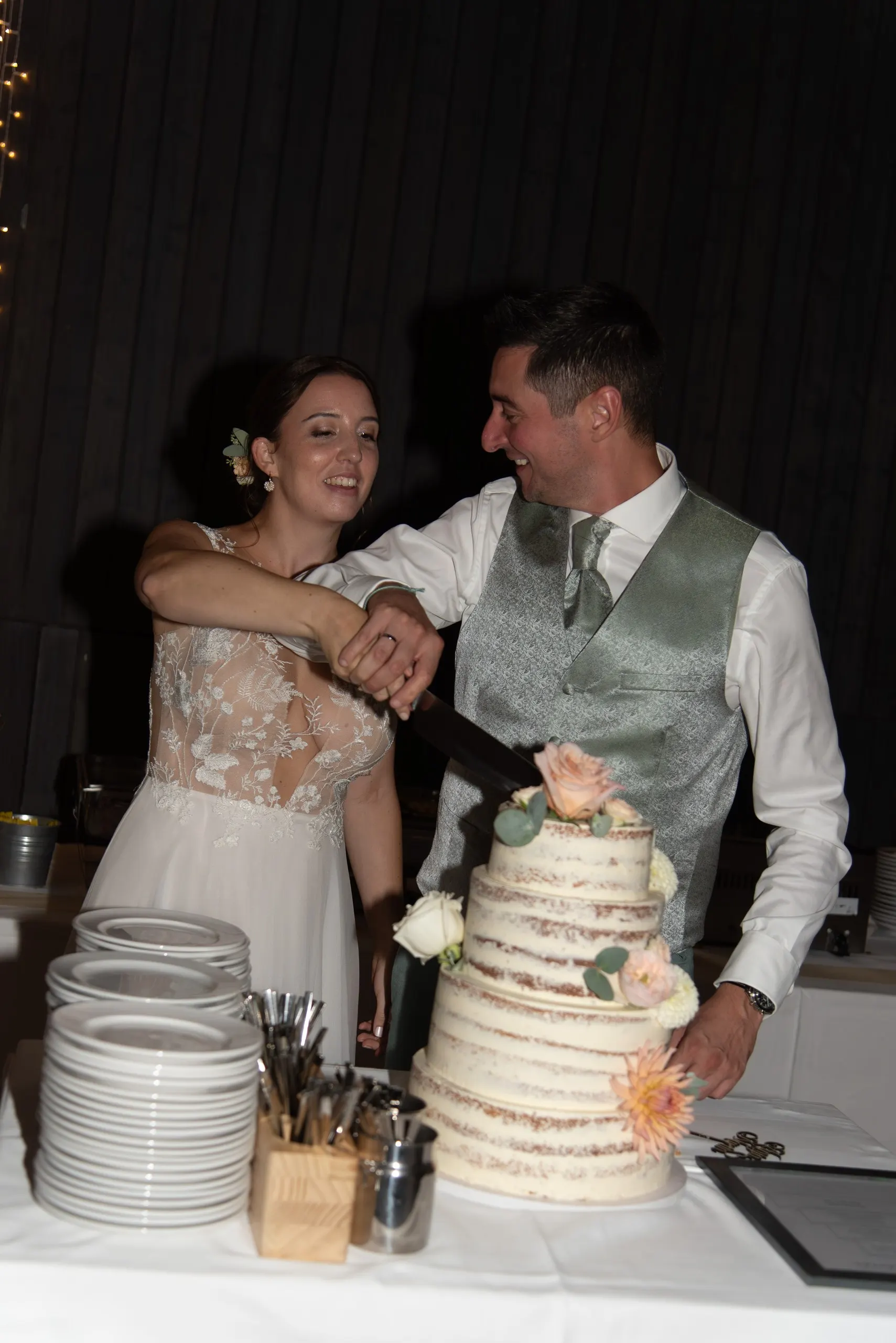 Anja und Martin schneiden gemeinsam die Hochzeitstorte an, er lacht sie dabei herzlich an