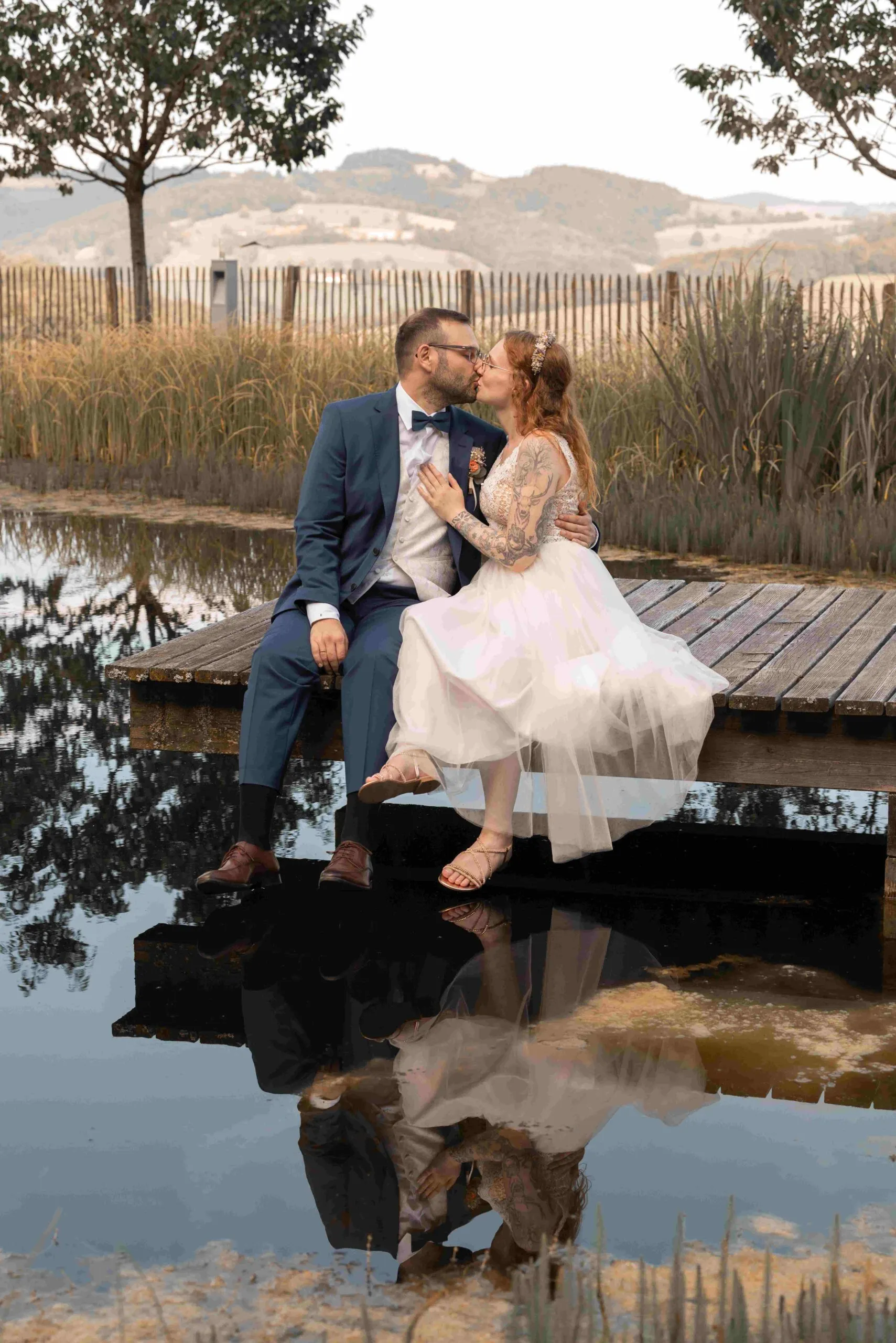 Chrisi und Andreas küssen sich am Stegrand, ihre Spiegelung liegt im dunklen Wasser des Teichs.