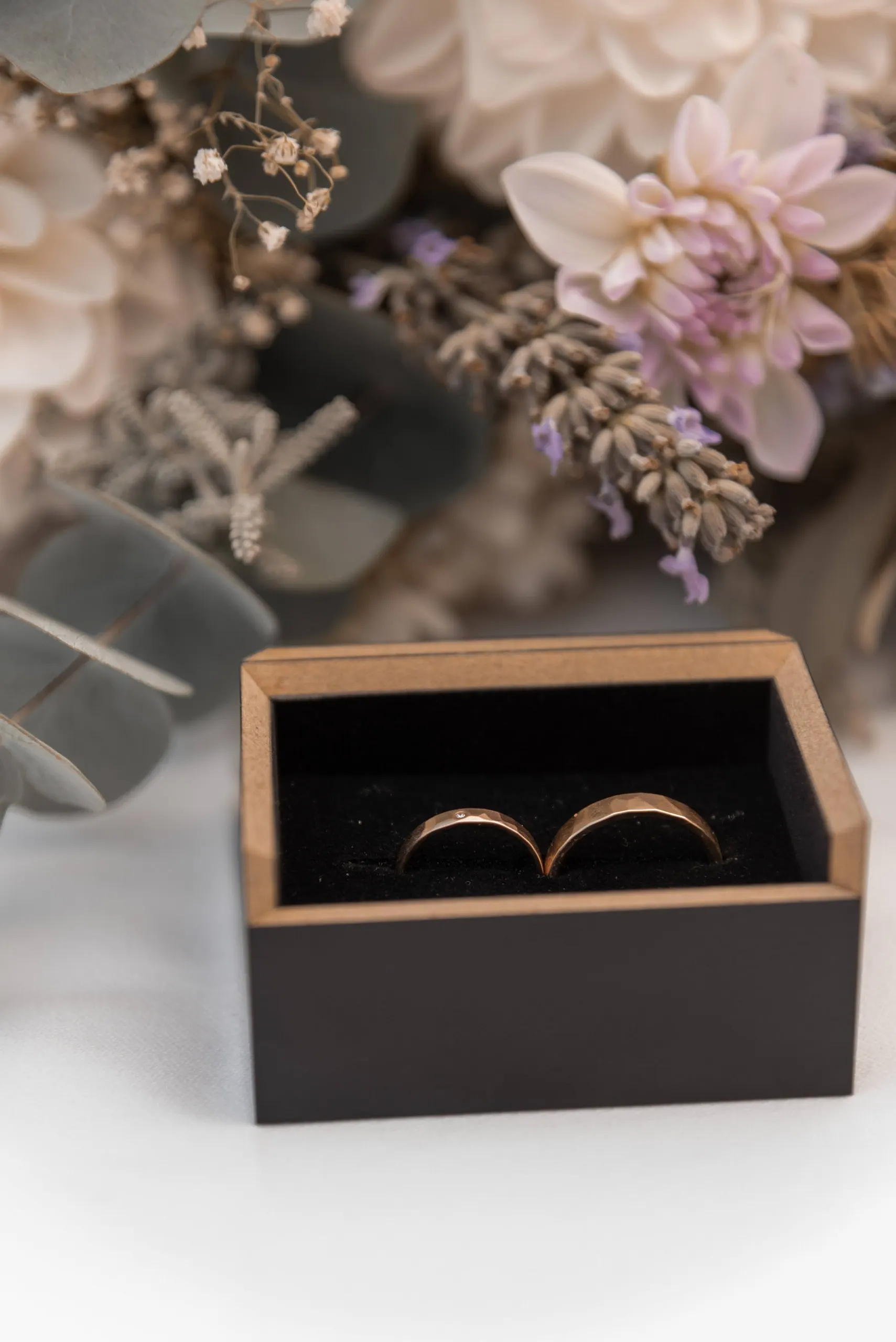 Geöffnete Ringschachtel mit zwei Eheringen, dahinter Trockenblumen