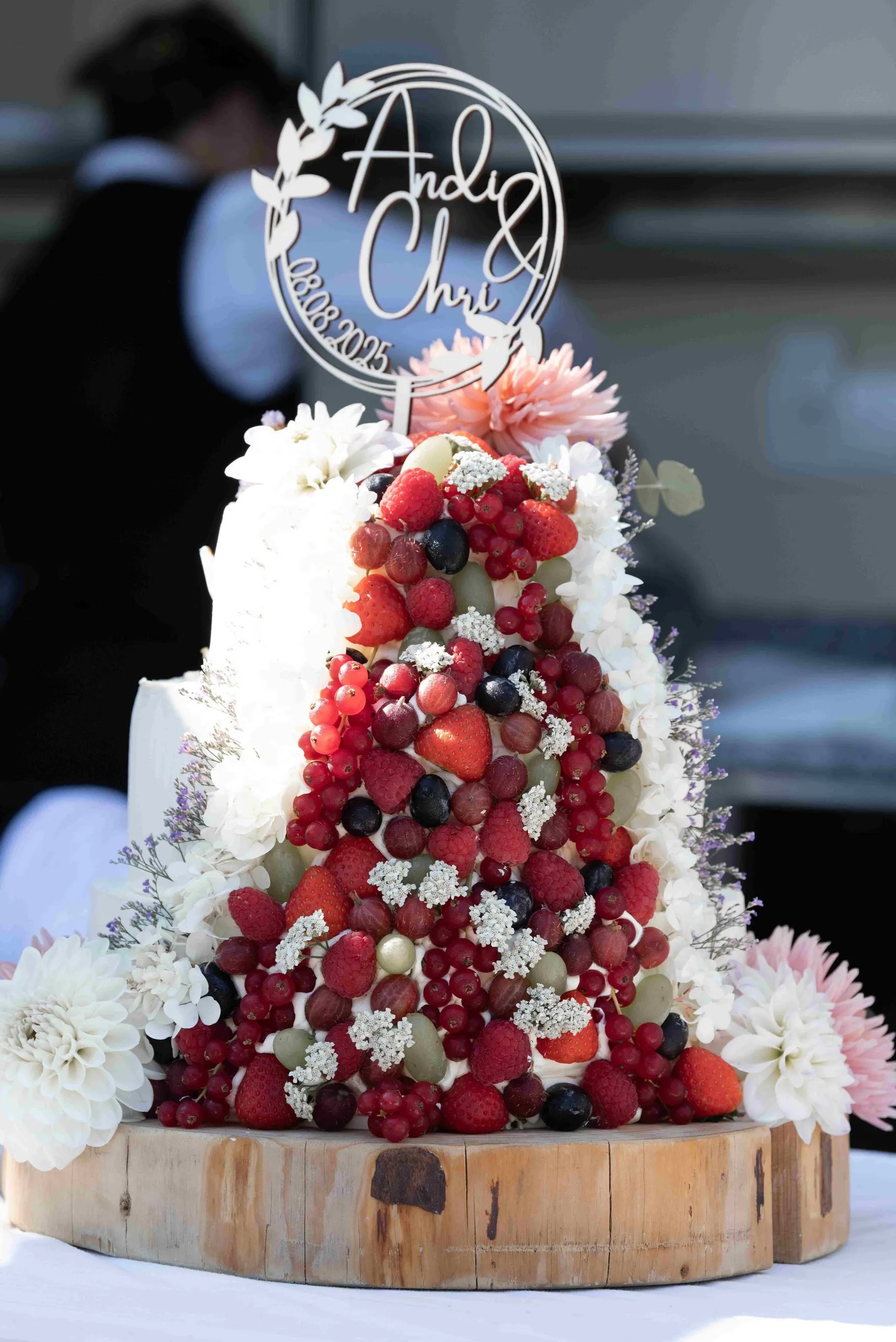 Hochzeitstorte mit Beeren und Blüten auf einer Holzscheibe