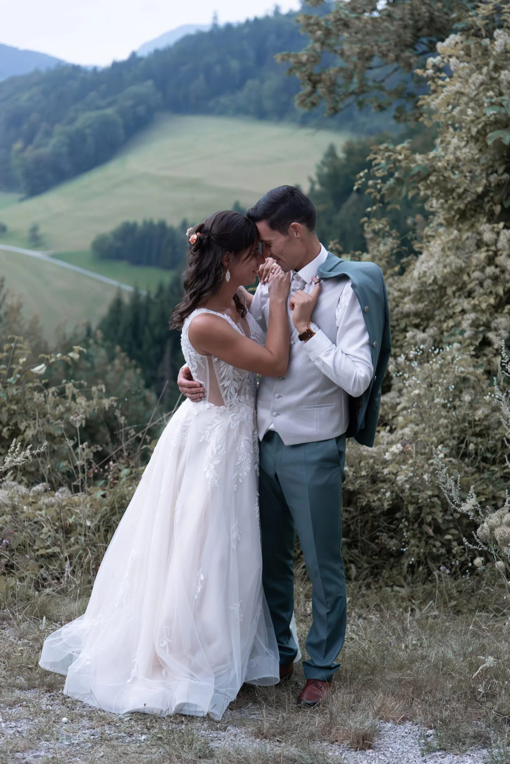 Stirn an Stirn stehen Elisa und Stefan vor der Hügellandschaft, das Sakko lässig über seiner Schulter