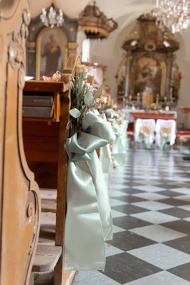 Der Mittelgang der Kirche mit Schachbrettboden, Blumenschmuck an den Bänken und Luster über dem Altar