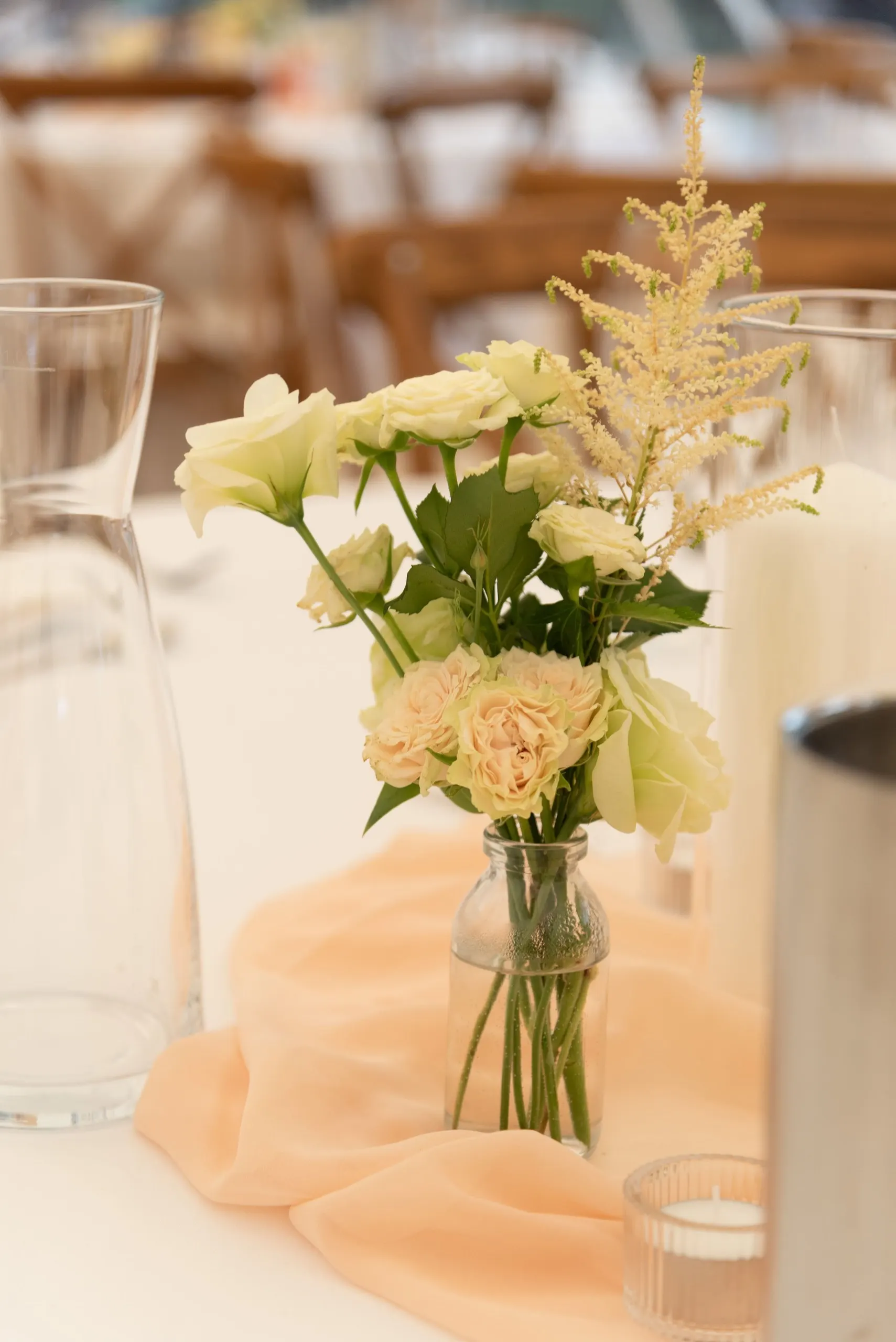 Tischschmuck im Festzelt: Rosen und Astilbe in einer Glasvase auf apricotfarbenem Chiffon