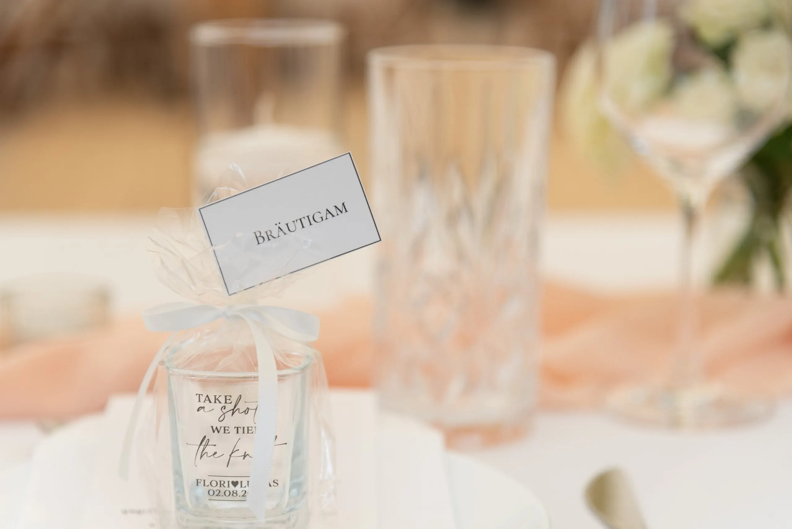 Tischkarte an einem Gastgeschenkglas, dahinter geschliffene Gläser
