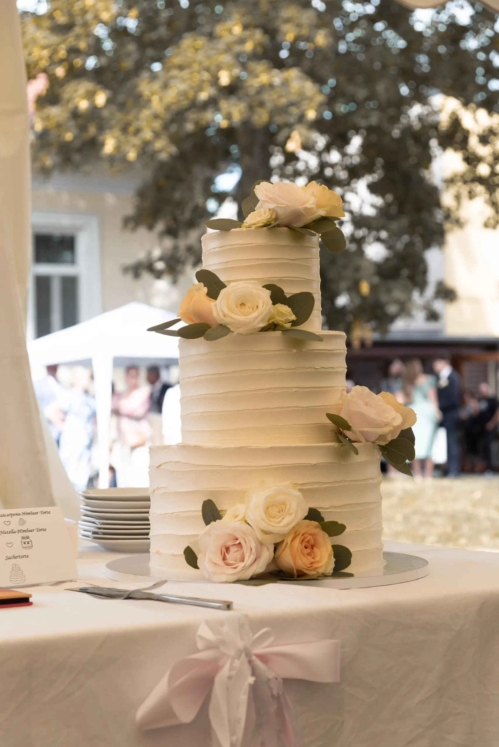 Die Hochzeitstorte mit Rosen im Garten, eine rosa Schleife am Tischtuch