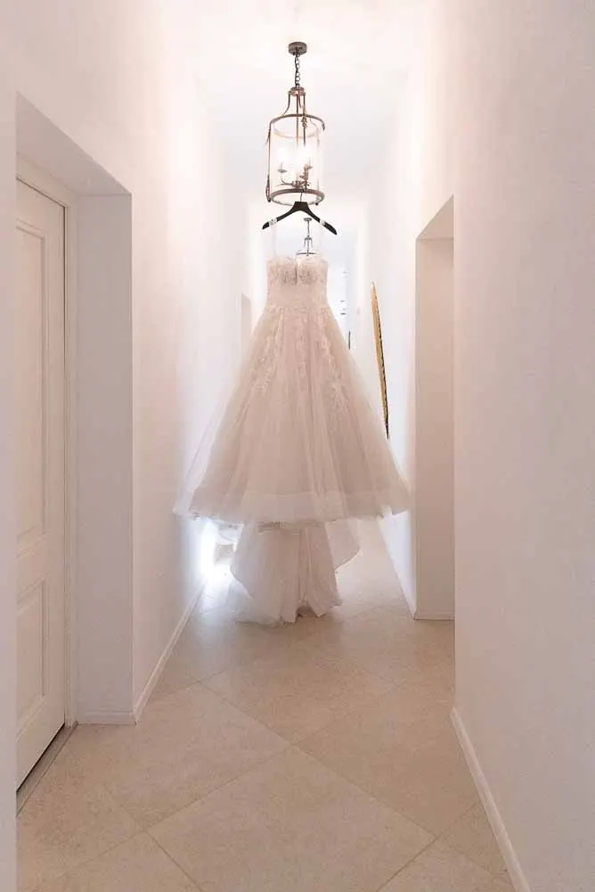 Das Brautkleid hängt im hellen Gang unter einem Luster