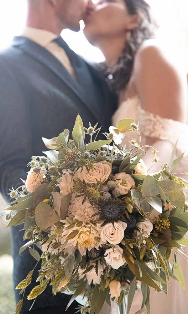 Brautstrauß aus Rosen und Herbstlaub vor dem küssenden Paar