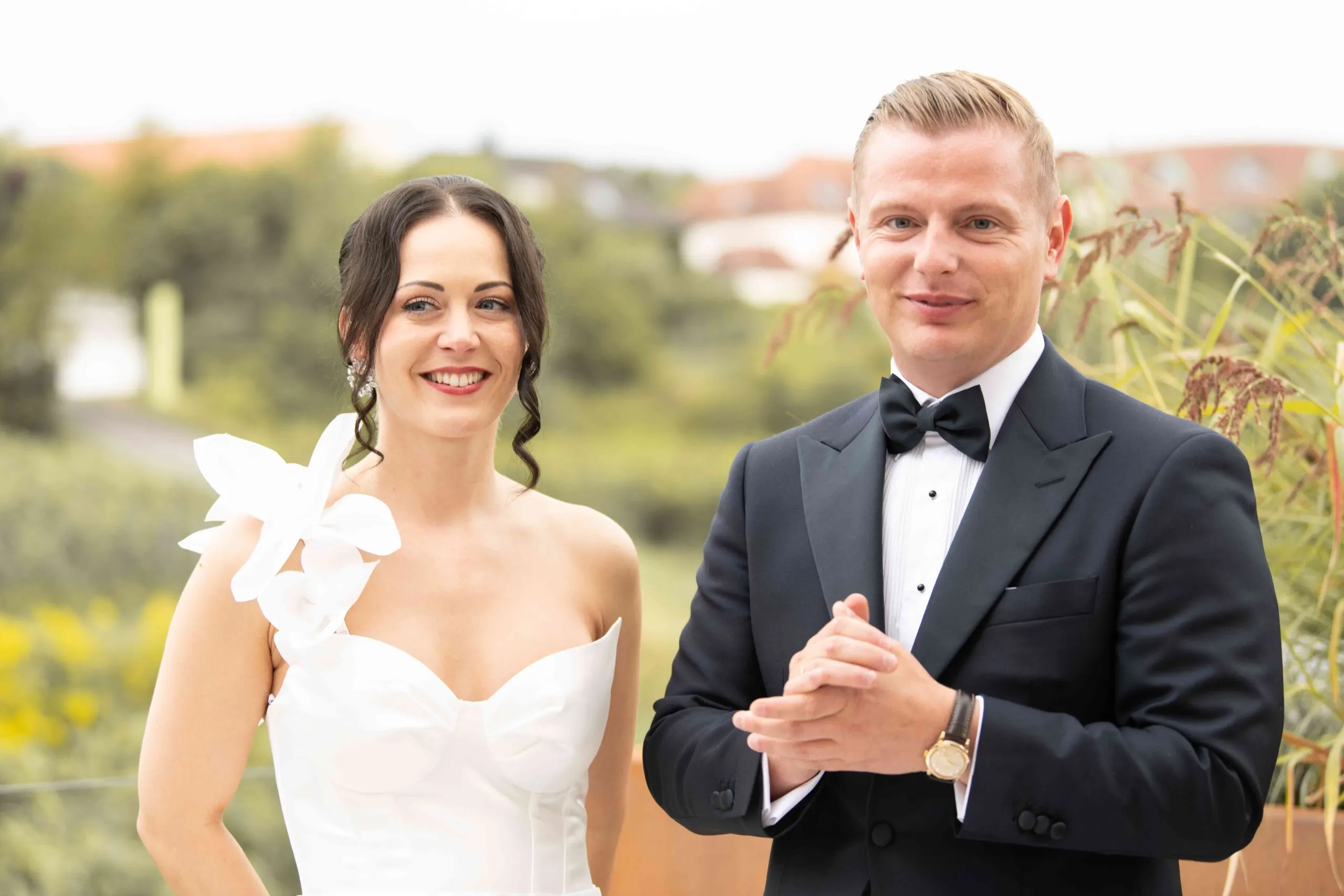 Ruhiges Porträt am Tortentisch: Julia und Denis nebeneinander, hinter ihnen wiegen sich Gräser
