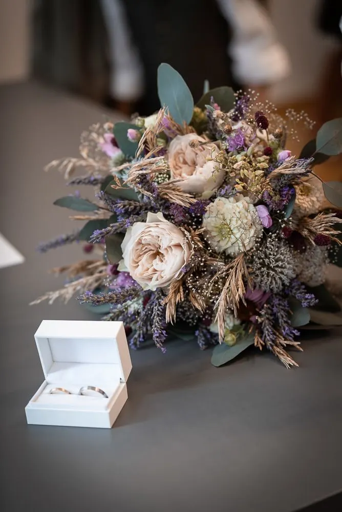 Brautstrauß aus Trockenblumen und Rosen neben der geöffneten Ringschachtel