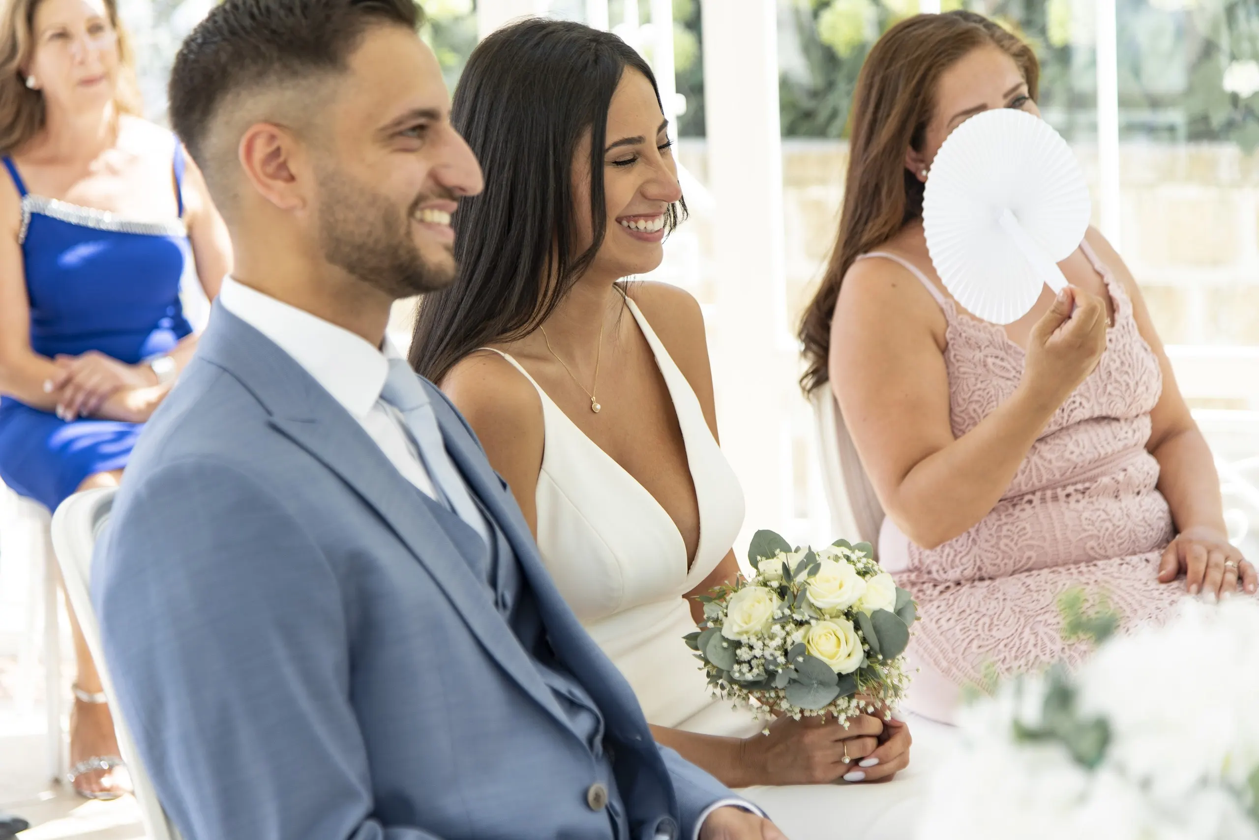 Bei der Trauung lachen Melissa und Benjamin mit der Trauzeugin in Rosé, die einen weißen Fächer hält