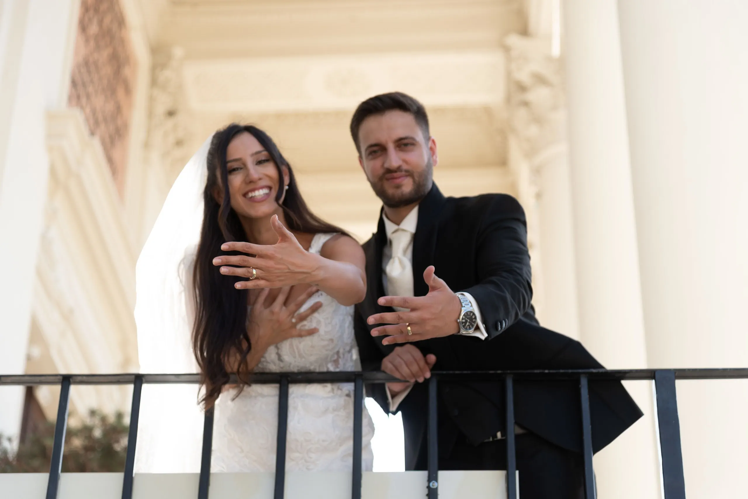 Unter dem Säulenportal der Karlskirche zeigen Melissa und Benjamin lachend die Ringe