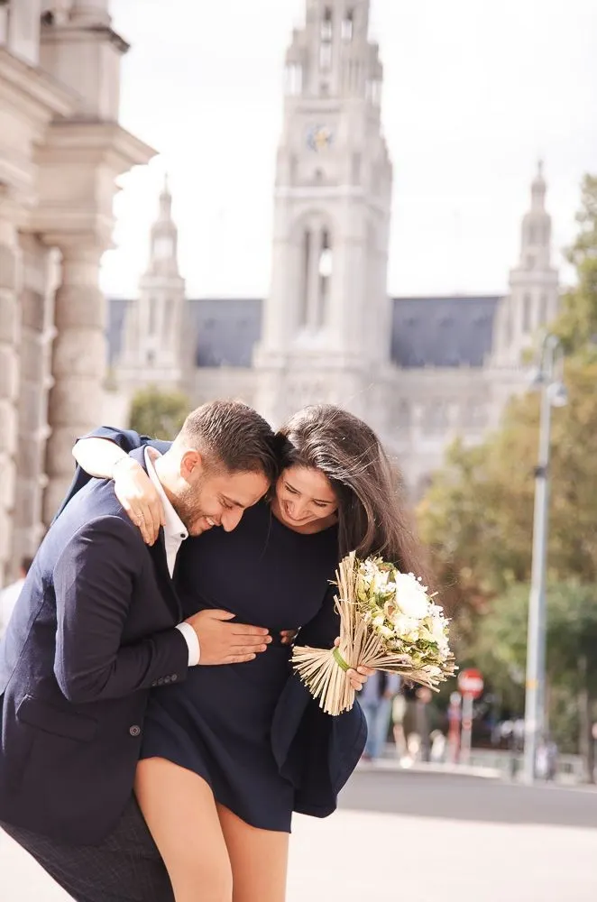 Verlobungsshooting: Melissa und Benjamin umarmen sich lachend, dahinter das Wiener Rathaus