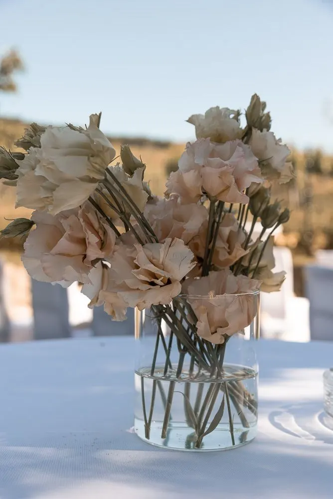 Strauß aus zartrosa Rosen in einer Glasvase, die Weinberge unscharf dahinter