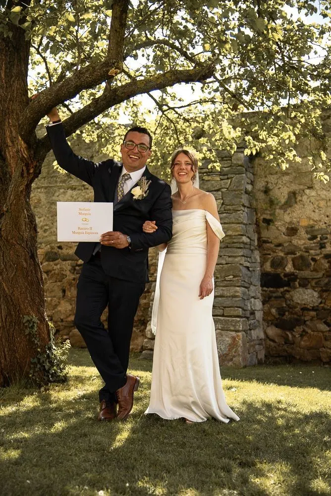 Ramiro hält die Urkunde hoch, Stefanie lacht neben ihm unter dem Baum