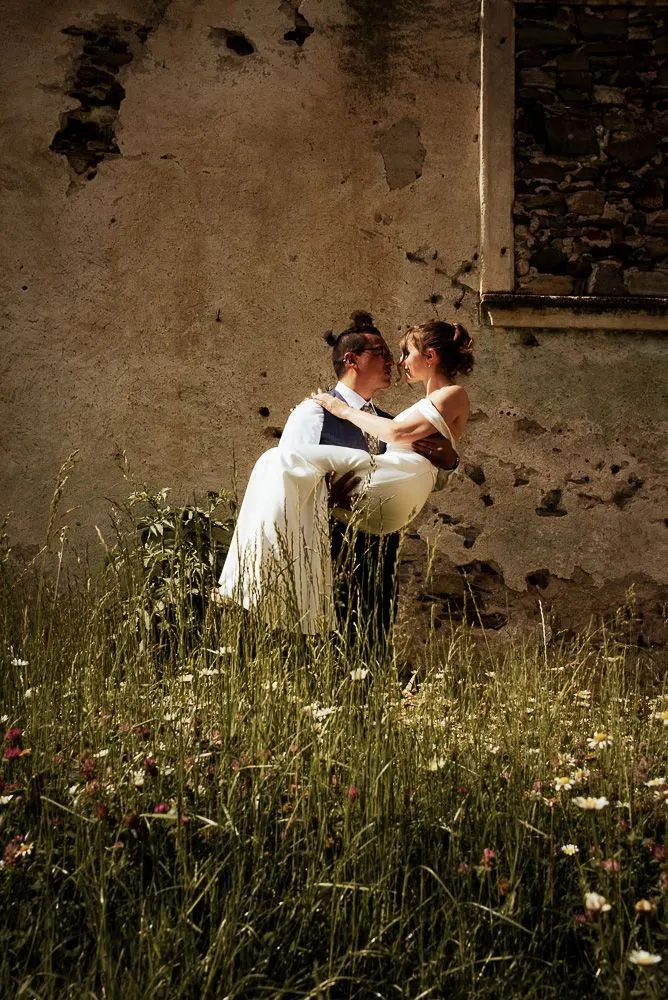 Ramiro hebt Stefanie hoch, Wiesenblumen vor der alten Mauer