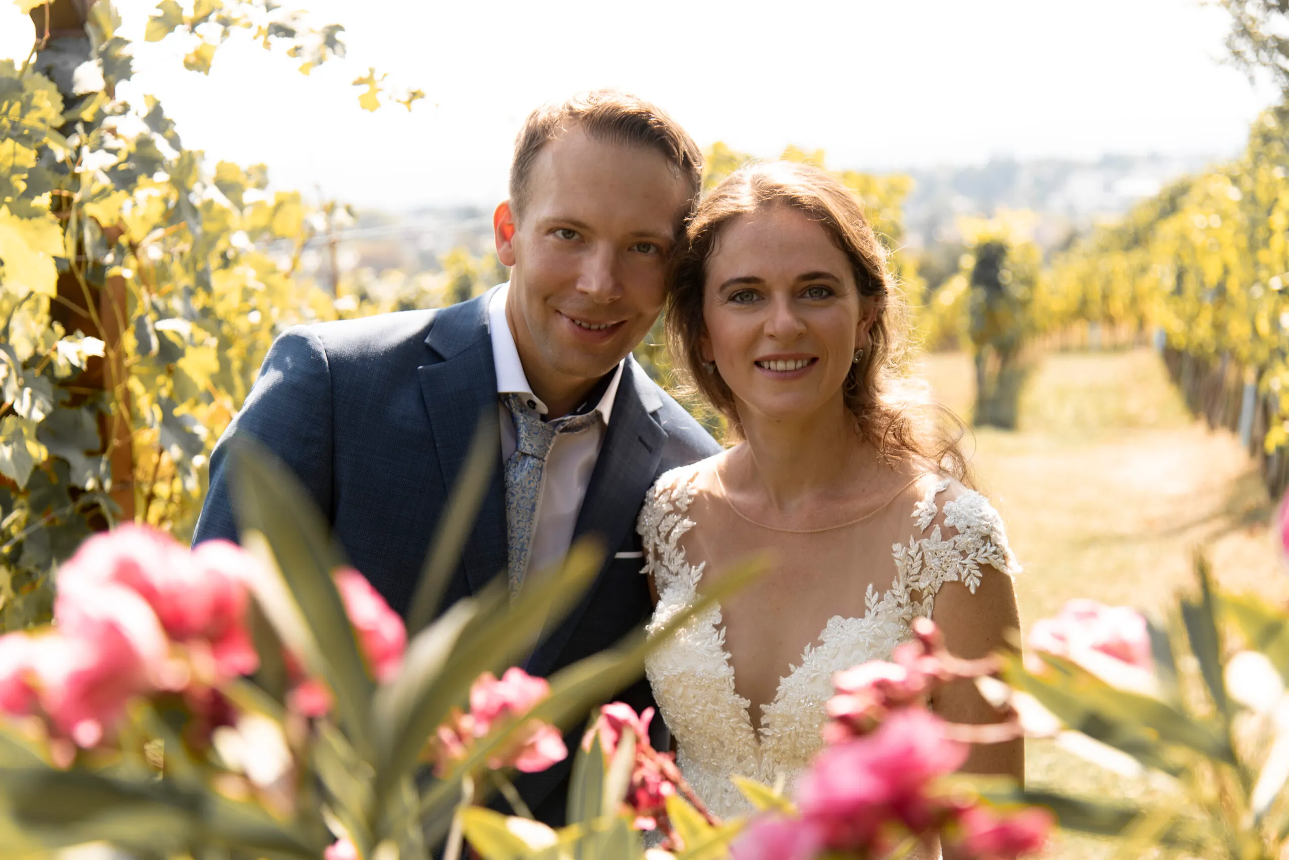 Karen und Sandor stehen zwischen Weinreben, im Vordergrund rosa Blüten