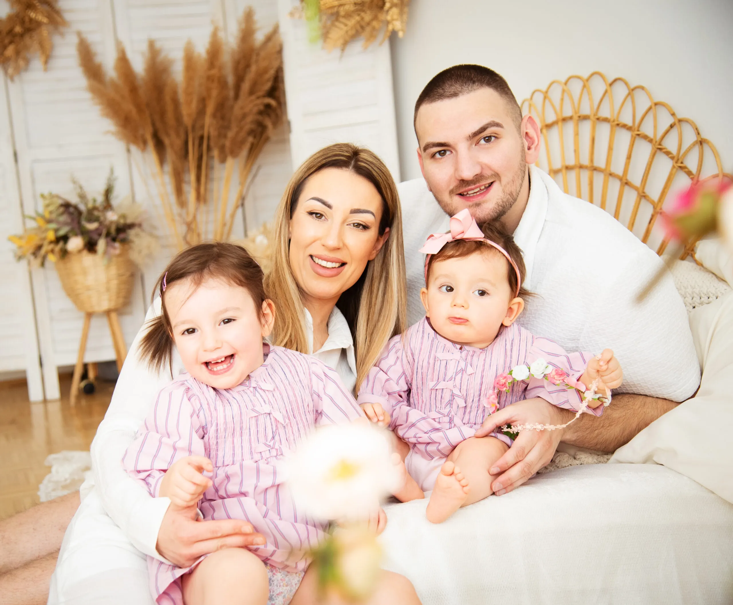 Eine vierköpfige Familie kuschelt lächelnd auf einem Bett, dahinter Pampasgras und ein heller Paravent.
